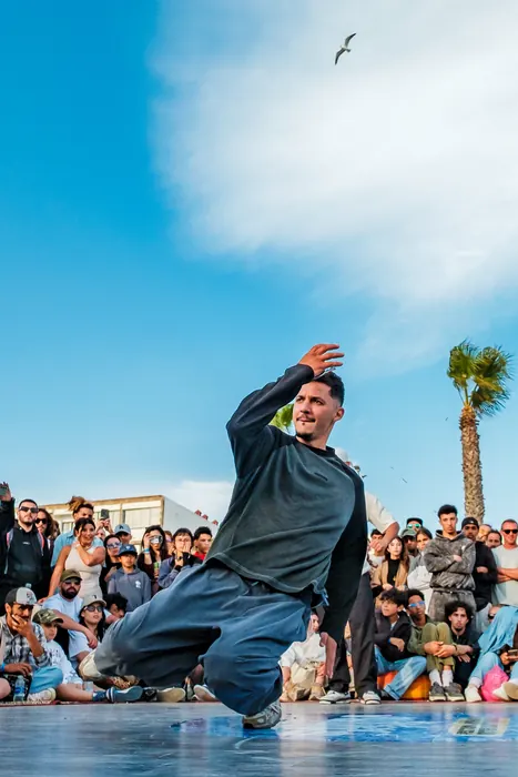 Un b-boy en appui bas sous le ciel bleu, la foule derrière lui