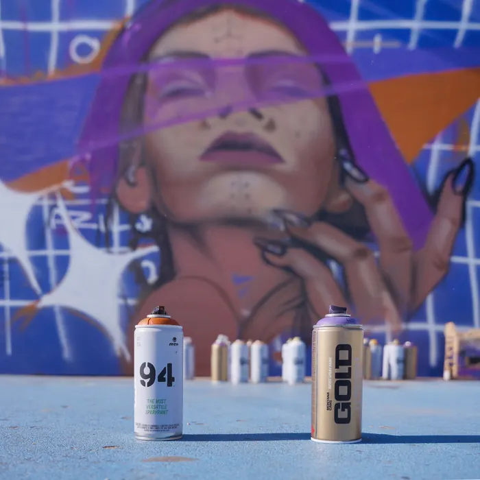 Deux bombes de peinture devant une fresque de visage de femme