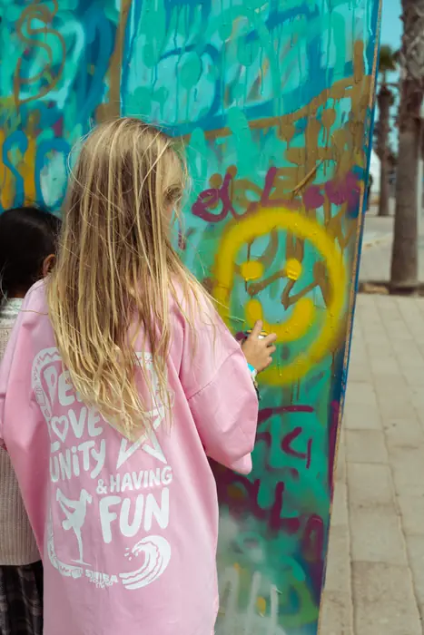Une enfant au sweat « Peace Love Unity Having Fun » peint sur un mur